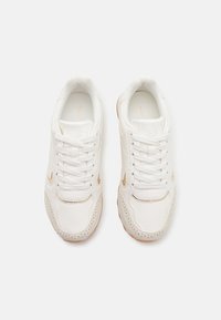 Baskets blanches avec une tige en cuir texturé, des accents dorés, des détails perforés et une semelle en caoutchouc, avec un système de laçage.