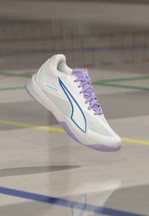 Witte en paarse sportsneaker met blauw logo en "ACCELERATE" tekst, zwevend boven een gymvloer met gekleurde veldlijnen.