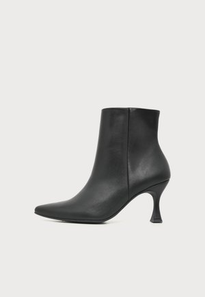 Bottine en cuir noir avec bout pointu et talon moyen courbé sur fond blanc.