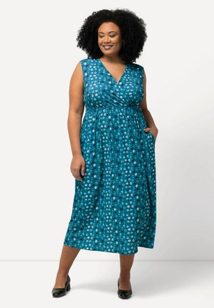 Vestido verde azulado con diseño cruzado, sin mangas, que presenta un patrón circular en tonos de azul y gris, con fruncido en la cintura y bolsillos.