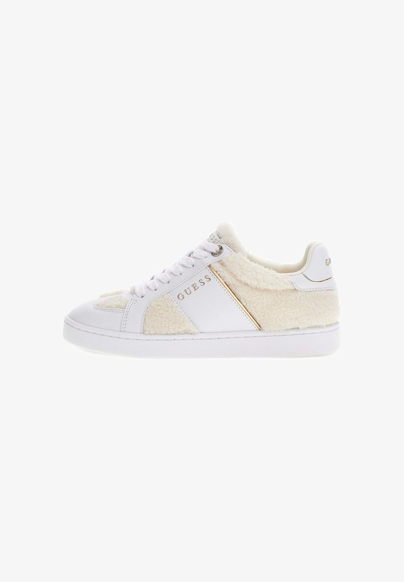 White sneaker featuring a plush, cream-colored shearling panel, gold accent, and white laces. Smooth texture with a round toe design.