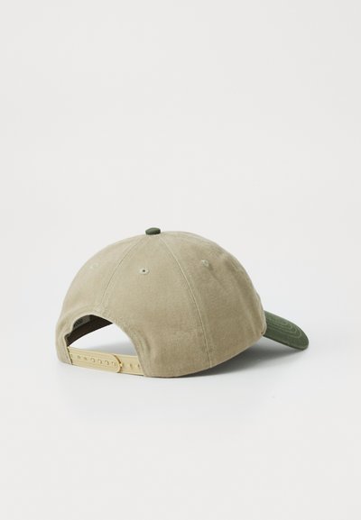 Gorra de tela beige con visera verde, correa ajustable color beige en la parte trasera, forma redondeada y un pequeño botón verde en la parte superior.