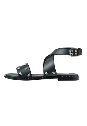 Zwarte platte sandaal met gekruiste enkelriemen, zilverkleurige stervormige studs op de voorriem en een zilveren gespsluiting aan de zijkant.