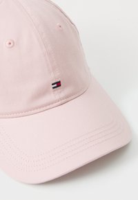Pink baseball cap made of cotton. Features a curved brim, stitched detailing, and a small logo with navy, white, and red accents.