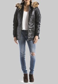 Giacca di pelle nera con spalle trapuntate, colletto di pelliccia sintetica, chiusura con zip, abbinata a jeans strappati blu sbiaditi e stivaletti marroni.