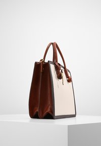Brązowa skórzana torebka z jasnobeżowym przednim panelem, o strukturalnym kształcie, z dwiema rączkami i małym akcentem w postaci klucza. Teksturowane boczne panele dodają detali.