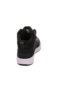 Sneaker alta nera con fodera in ecopelliccia, parte superiore in pelle liscia e tessuto, dettagli testurizzati e suola in gomma bianca. Presenta il marchio Adidas.