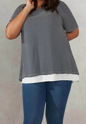Sort-hvid stribet kortærmet top lagdelt over et hvidt underlag, parret med blå denimbukser. Blødt, letvægtsstof med en afslappet pasform.