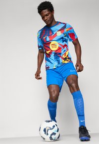 Kék sportmez, több színű absztrakt mintákkal és logóval, kék sorttal és zoknival párosítva. Fekete cipő és focilabda is tartozik hozzá.