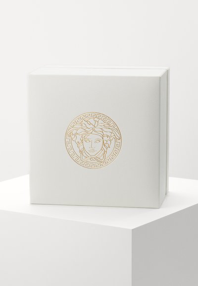 Vit låda med texturerad yta, prydd med en guldprägling av Medusa-logotypen i en cirkulär design med accenter av grekisk nyckelmönster.