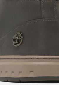 Dunkelgraue Lederstiefel mit gestickten Akzenten und einem signaturgeprägten Baumlogo. Helle beige Gummisohle mit strukturierter Griffigkeit.