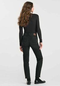 Jean noir, coupe slim, taille haute, avec un patch en cuir à l'arrière et des coutures discrètes. Associé à un haut à manches longues noir.