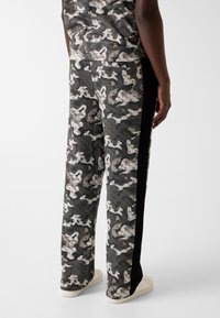 Cargobroek met camouflageprint in donkergrijs met witte accenten, gemaakt van zachte stof, met een rechte pijp en zwarte zijpanelen.