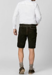 Pantalones cortos de cuero marrón oscuro con bolsillos laterales, detalles cosidos, combinados con calcetines de lana grises y zapatos marrones. Camisa blanca de botones visible.