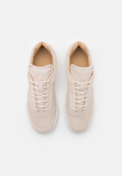 Zapatillas de ante beige con diseño bajo, punta redonda y suela de goma blanca. Presentan cordones tonales y un logo embossado en la lengüeta.
