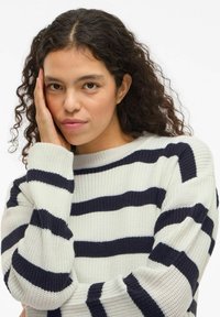 Pull en tricot crème avec rayures horizontales bleu marine, doté d'un col rond et de manches amples, mettant en valeur un tissu texturé.