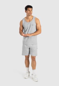 Top sin mangas gris y pantalones cortos de tejido suave. El top tiene un cuello redondo y un pequeño logotipo. Combinado con zapatillas blancas y calcetines.