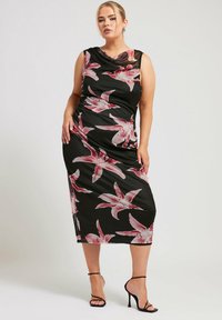 Musta kukallinen mekko, jossa on vaaleanpunaisia liljakuvioita, hihaton malli, kaareva kaula-aukko ja polveen ulottuva leikkaus, täydentäen asua mustilla remmikenkillä.