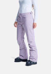 Helle lila Skihosen mit tailliertem Design, ausgestattet mit seitlichen Reißverschlusstaschen und verstärkten Bündchen. Tragen mit schwarzen Skischuhen auf einem weißen Hintergrund.