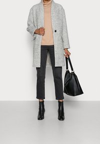 Szary płaszcz w jodełkę z pojedynczym guzikiem, beżowy golf, czarne jeansy o prostych nogawkach i czarne skórzane botki, trzyma torbę typu tote w kolorze czarnym.