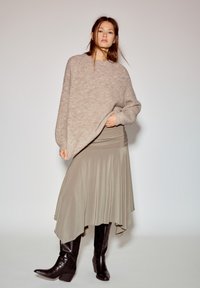 Béžový pletený sveter s voľným strihom, v kombinácii s prúdiacou taupe sukňou a čiernymi koženými priliehavými čižmami. Jednoduché a vrstvené dizajnové prvky.