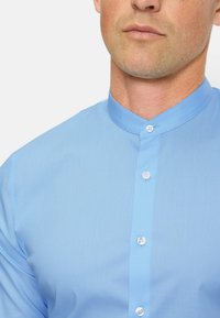 Lichtblauw, overhemd met lange mouwen en een Mandarijnkraag, met een gladde textuur en twee knoopsluitingen bij de hals.