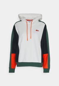 Felpa con cappuccio caratterizzata da un corpo bianco, pannelli laterali verdi e neri, dettagli arancioni e un piccolo logo ricamato sul petto.