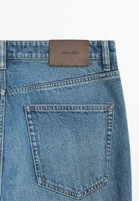 Poche arrière d’un jean en denim bleu avec des coutures visibles et une étiquette en cuir marron embossée du nom de la marque Massimo Dutti.
