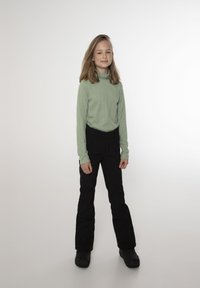 Maglia a maniche lunghe ribassata verde chiaro, pantaloni da sci neri e stivali neri. La maglia ha un collo alto e maniche aderenti, mentre i pantaloni sono a gamba dritta.