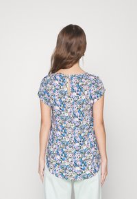 Blusa floreale in colori pastello, con scollatura tonda, maniche corte e dettaglio a chiave sulla schiena. Tessuto leggero con un design fluido.