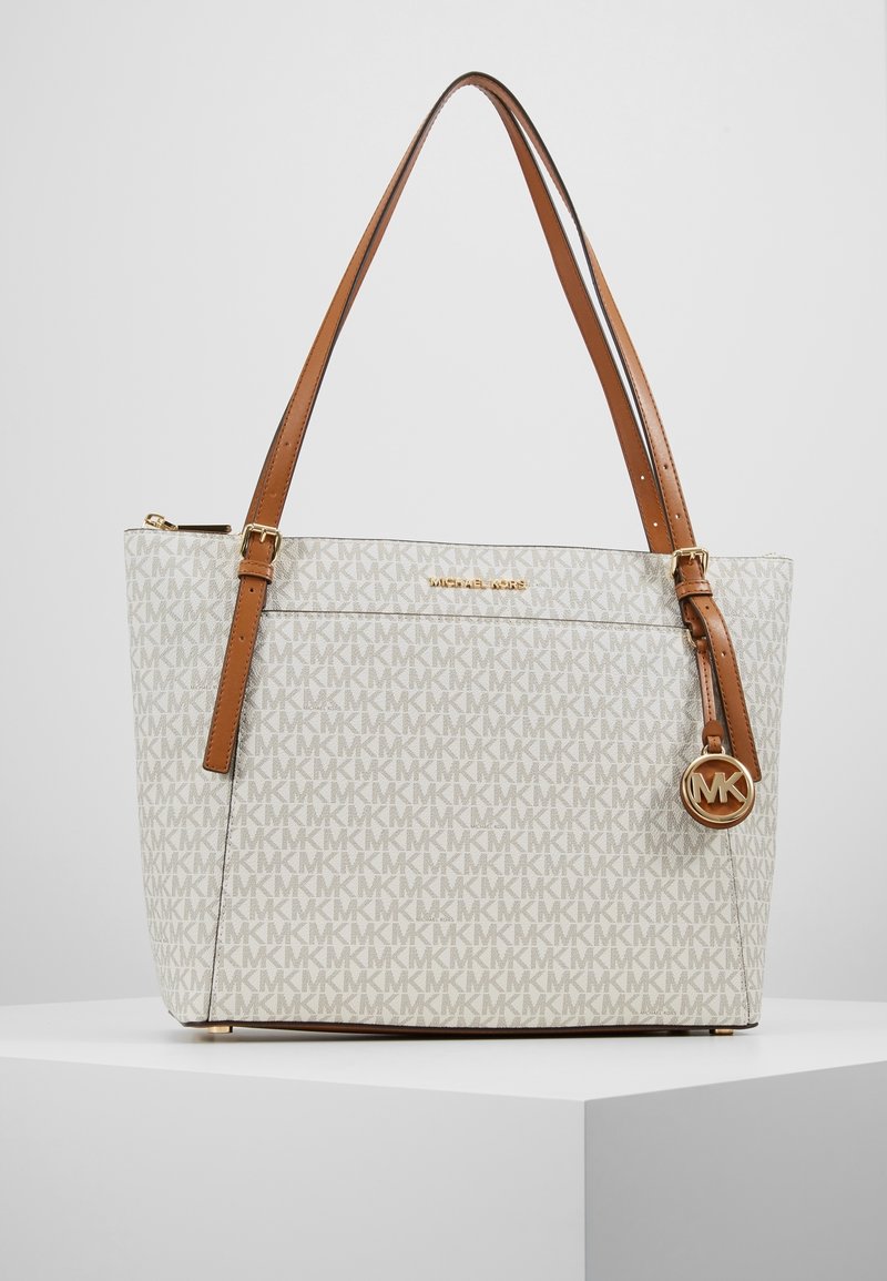Sac cabas beige et marron Michael Kors avec motif monogramme MK, bandoulières réglables et breloque logo MK dorée sur une surface blanche.