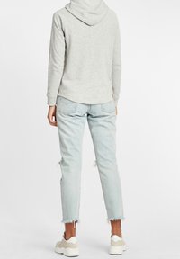 Felpa grigia chiara con un motivo testurizzato, abbinata a jeans in denim chiaro strappati. Sneakers bianche con dettagli beige completano l'outfit.