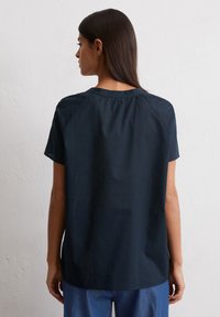 Navy blue short-sleeve top with a loose fit, round neckline, and back pleat detail. Soft fabric with a smooth texture.