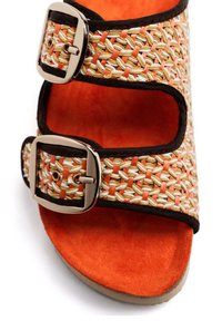 Sandale à glissière tissée en matériau orange, crème et tan, avec deux boucles métalliques réglables. Semelle intérieure en daim orange doux. Semelle en caoutchouc plate.