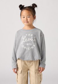 Sudadera gris de manga larga con escote redondo, que presenta un logo blanco de Levi's. Combinada con pantalones cargo color caqui con bolsillos laterales.