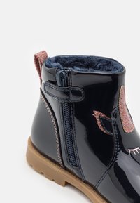 Námořnické lakované kotníkové boty s umělou kožešinou, třpytivý růžový akcent, boční zip a gumová podrážka. Detail s emblémem srdce a oka.