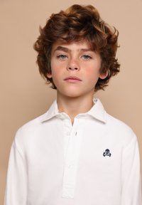 Weißes Langarm-Polohemd mit Button-Down-Kragen, Knopfleiste und einem marineblauen Totenkopf- und gekreuzten Schenkeldetail auf der Brust.