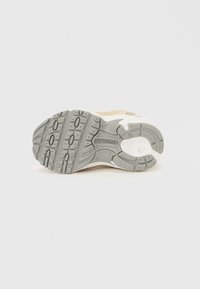 Αθλητικό παπούτσι σε ανοιχτό μπεζ με υφή στην γκρι λαστιχένια σόλα, που διαθέτει αυλάκια για πρόσφυση και λογότυπο στο πίσω μέρος.