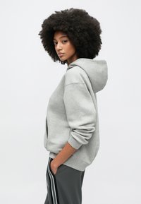 Hall halli kapuutsiga pusa, mis on valmistatud pehmest kangast, varustatud avara kapuutsiga, soonikkoes varrukasäärte ja vöökohataskutega. Kandmiseks koos tumedatehallide küljeribadega pükstega.