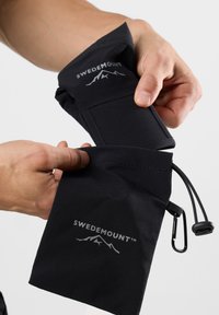 Black fabric pouch with logo, featuring a drawstring closure and clip. Hands demonstrate opening pocket for storage. Smooth texture.
