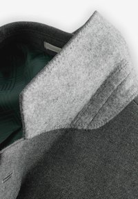 Gulerul jachetei gri prezintă o căptușeală moale din fetru gri și un material texturat de culoare gri închis. În interior se observă un material cu un model verde. Cusături îngrijite.