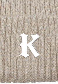 Căciulă tricotată bej cu textură în dungi, având un logo proeminent pe culoarea argintie "K" în față. Material moale și călduros.