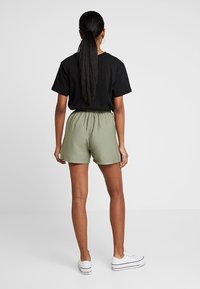 Černé tričko s krátkým rukávem spárované se světle zelenými šortkami s elastickým pasem. Celý outfit doplňují bílé tenisky.