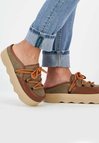 Scarpe casual verdi e marroni con una suola spessa e ondulata di colore beige. Presentano lacci e cuciture arancioni, realizzate in materiali scamosciati e sintetici.