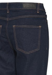 Jean en denim bleu foncé avec une texture lisse, présentant des surpiqûres orange contrastantes, deux poches arrière, et une étiquette logo noire à la ceinture.