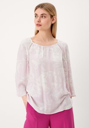 Blouse rose clair avec motif floral, tissu fluide, manches trois-quarts et décolleté carré, assortie à un pantalon fuchsia.