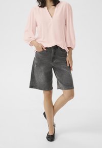 Lys pink, struktureret bluse med V-hals og trekvartærmer; parret med grå denim shorts og sorte flade sko.
