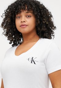 Biała koszulka V-neck wykonana z bawełny. Posiada szare logo Calvin Klein Jeans na lewej piersi. Miękka struktura z krótkimi rękawami.