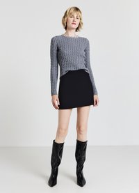 Maglione grigio a trecce con maniche lunghe, abbinato a una mini gonna nera e stivali neri con tacco al ginocchio. Presenta un collo rotondo con decorazioni di perle.