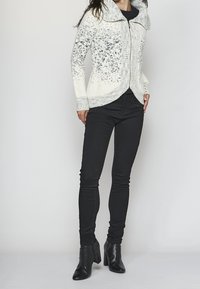 Stickad tröja i vitt med gråa prickar, med hög krage, dragkedja fram och ribbade ärmslut. Bärs med svarta slim-fit jeans och klackboots.